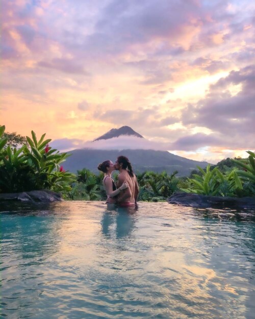 Piscoandbier couple kissing in hot springs of The Springs Resort and Spa in Costa Rica in front of volcano El Arenal during sunset