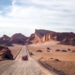 Red car driving in moonlike landscape towards the great wall of Valle De La Luna in the Atacama desert, Chile