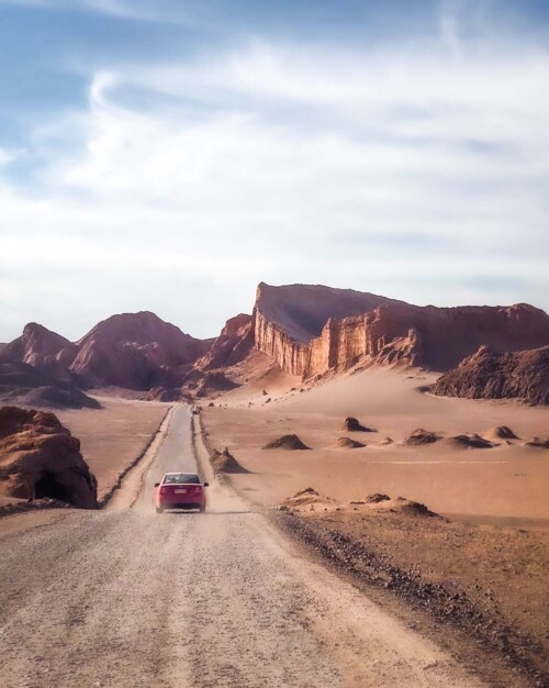 Red car driving in moonlike landscape towards the great wall of Valle De La Luna in the Atacama desert, Chile